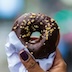 chocolate donut held in a person's hand'